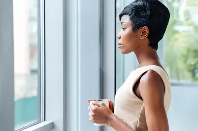 posh young black woman with short hair looking out of a window while holding a coffee or tea
