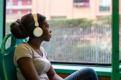 young black woman thinking traveling and listening to large headphones on a train