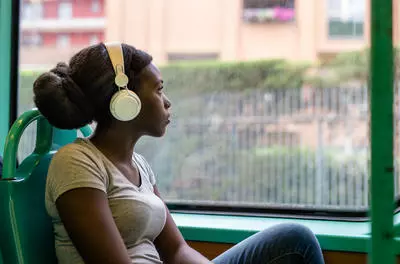 young black woman thinking traveling and listening to large headphones on a train