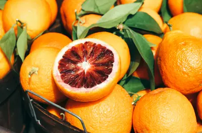pile of blood oranges with one cut open to reveal its red inside