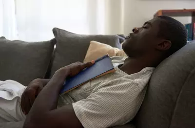 man napping on a couch with a book open on his chest