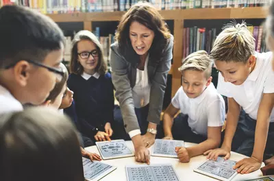 teacher standing at a table pointing to a lesson with students around her