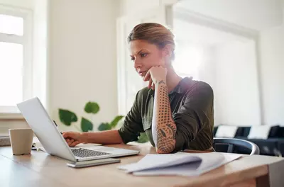 tattooed woman seriously contemplating options on a laptop