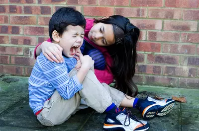young girl hugging her brother, who is crying after hurting his knee