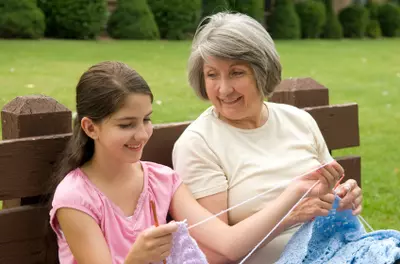 senior citizen teaching girl to knit