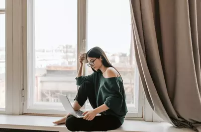 girl sitting by window looking at computer screen