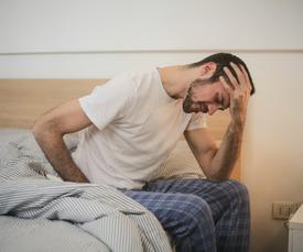 Guy sitting on bed in pain and holding head