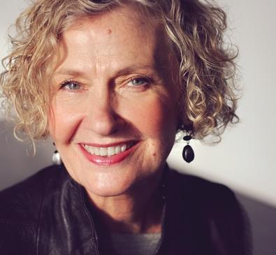 Ruth Bachman, an elder woman wearing earrings with blonde curly hair.