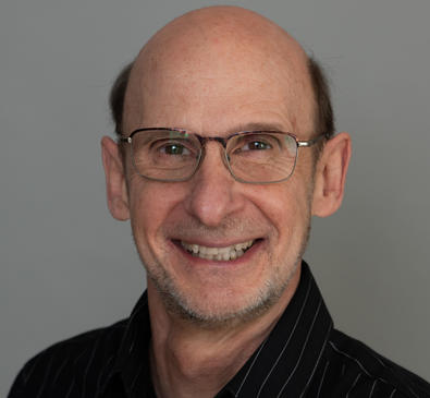 Steve Buechler, an elder man with glasses wearing a black button up and smiling