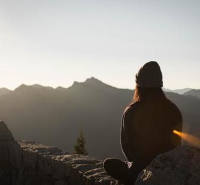 silhouette of a person wearing a beanie looking into the sunset over a landscape