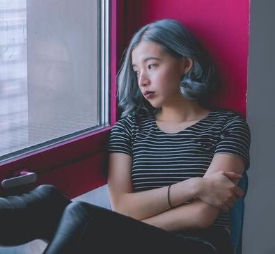 person in striped shirt looking out the window with crossed arms