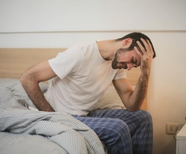 Guy sitting on bed in pain and holding head